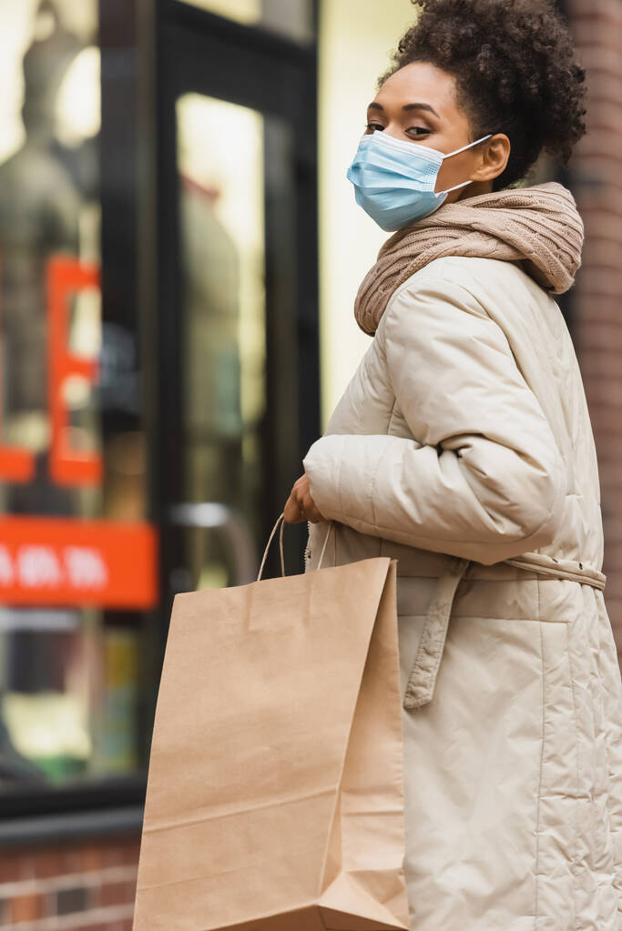 brunette african american woman in medical mask holding shopping bag - Photo, Image