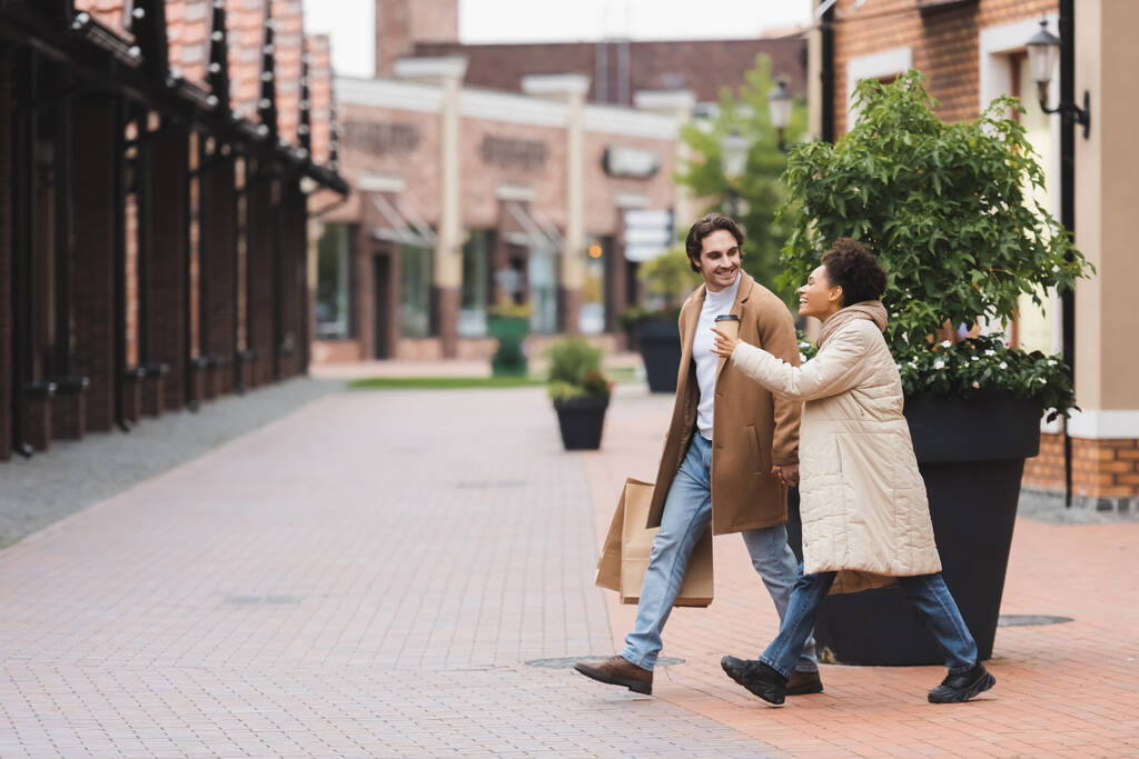 mulher americana africana alegre apontando com o dedo perto do namorado enquanto caminhava perto do shopping - Foto, Imagem