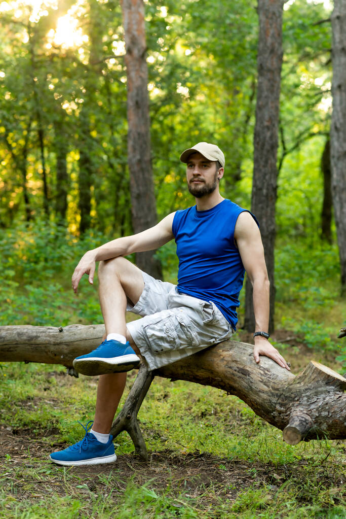 Joven barbudo descansando sobre un tronco en el bosque. Descanso verano. - Foto, imagen