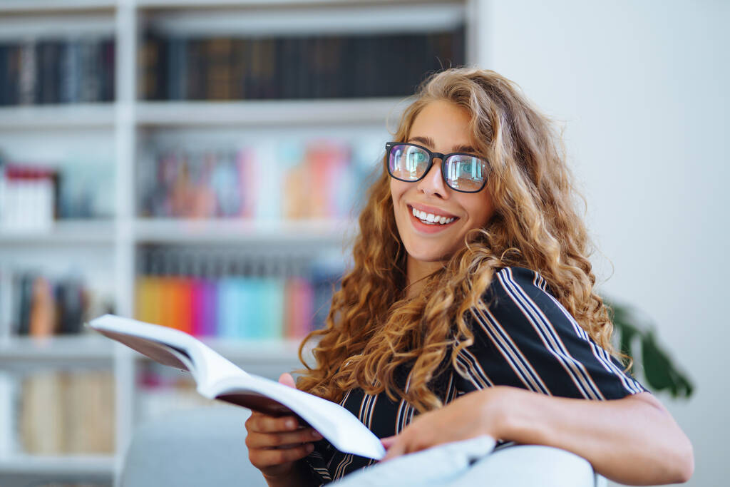 Egy fiatal nő ül egy könyvvel, laptok a könyvtárban és jegyzetel. Az oktatás fogalma, könyvtár, hallgatók.  - Fotó, kép