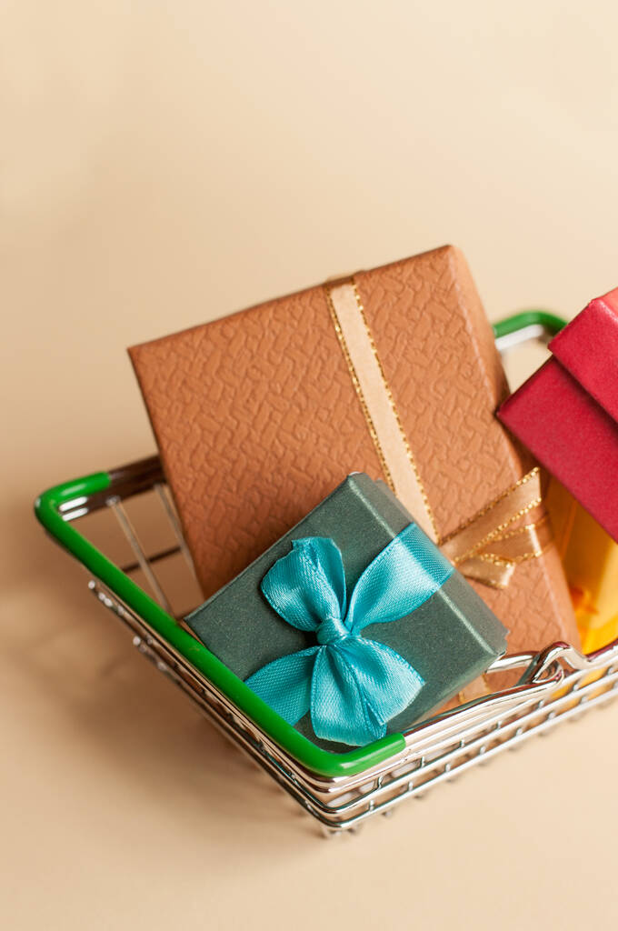 Bunte Geschenkboxen mit Schleifen in einem Metallkorb auf beigem Hintergrund im vertikalen Format - Foto, Bild