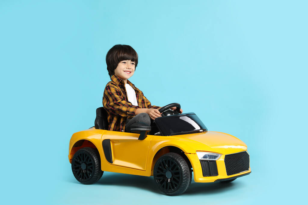 Niño pequeño conduciendo coche de juguete amarillo sobre fondo azul claro - Foto, imagen