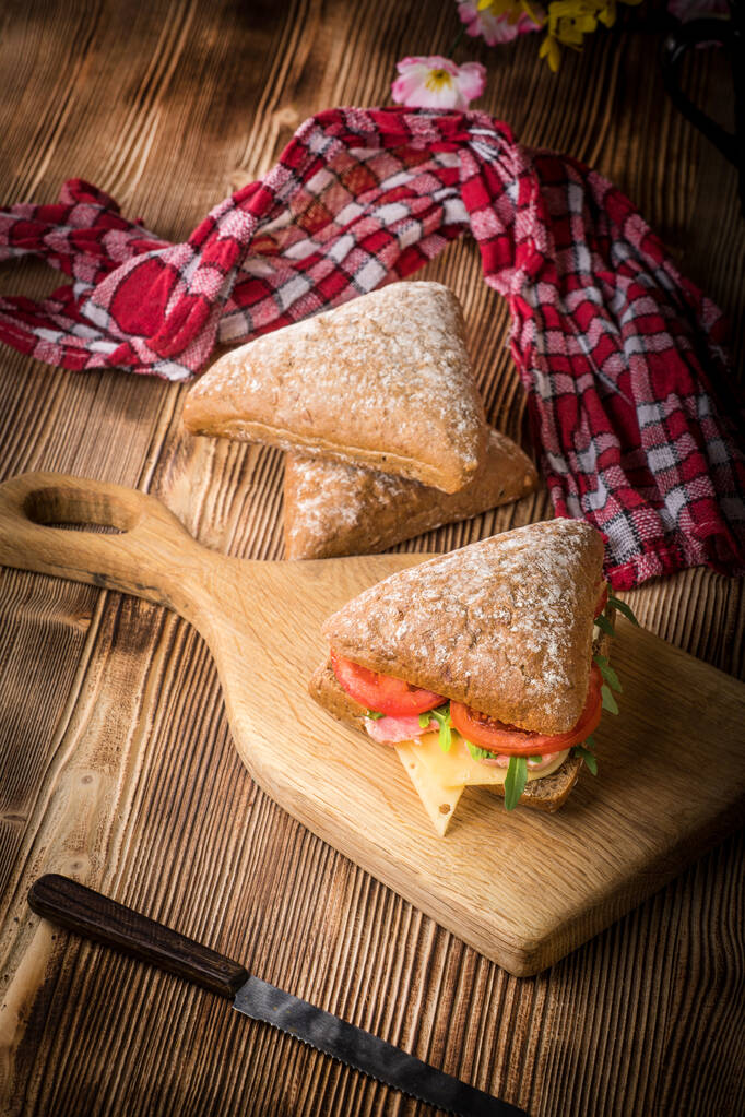 Sandwich triangular con queso, jamón y tomate sobre una mesa de madera
. - Foto, Imagen