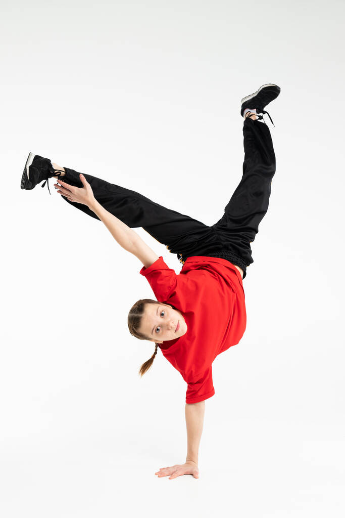 Eristetty nuori venäläinen tyttö hip hop break tanssija tanssii harmaa studio tausta, suorittaa jäädyttäminen downrock breakdance - Valokuva, kuva