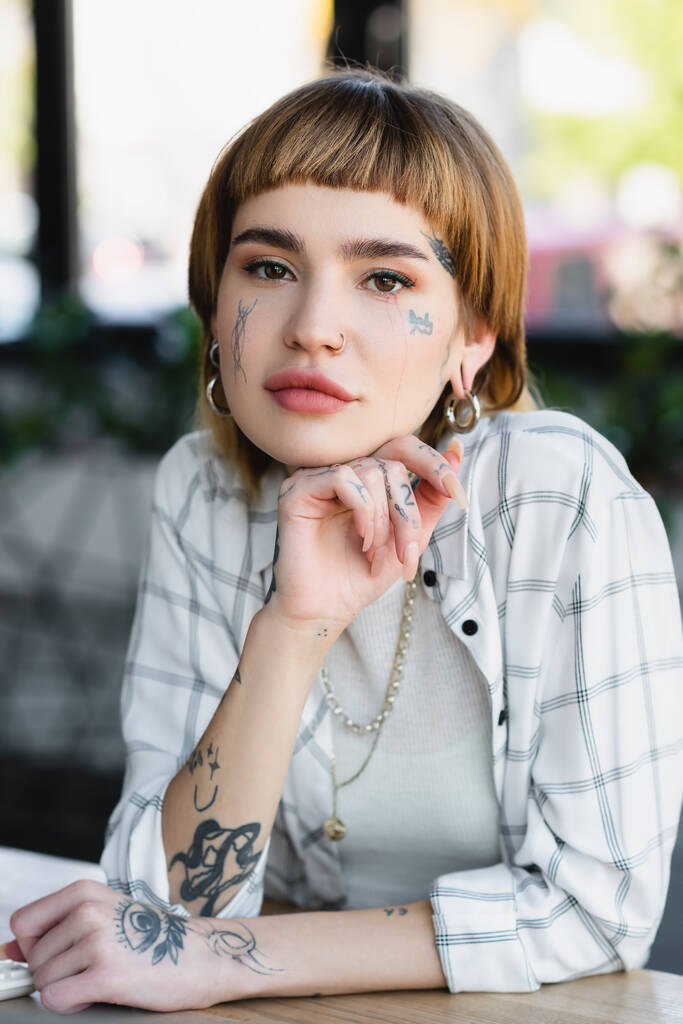 stylish tattooed businesswoman looking at camera while sitting in office - Photo, Image
