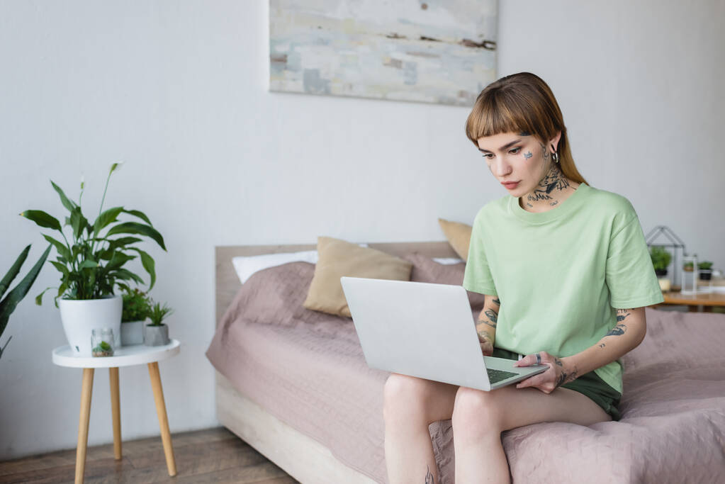 mladá žena s tetováním pomocí notebooku, zatímco sedí na posteli doma - Fotografie, Obrázek