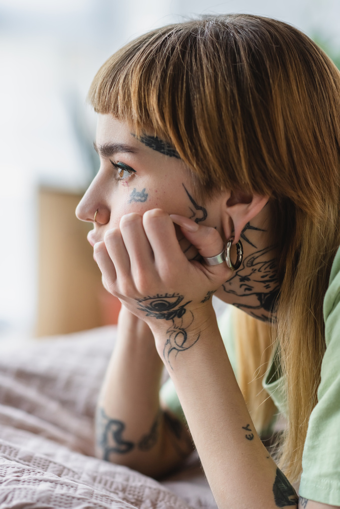 vista lateral da mulher tatuada com piercing olhando para longe na cama em casa - Foto, Imagem