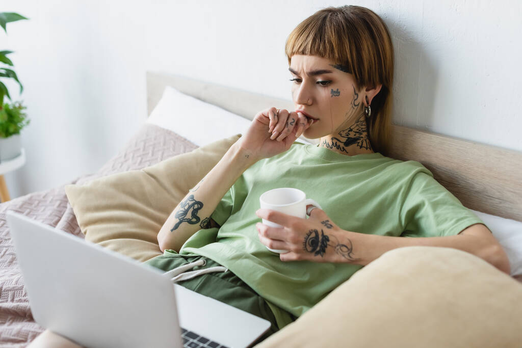 joven mujer preocupada con el cuerpo tatuado viendo la película en el ordenador portátil borroso - Foto, Imagen