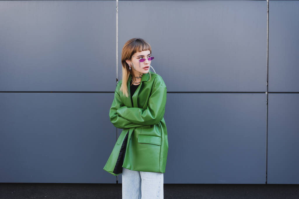 Tätowierte Frau in grüner Lederjacke mit verschränkten Armen im Freien - Foto, Bild