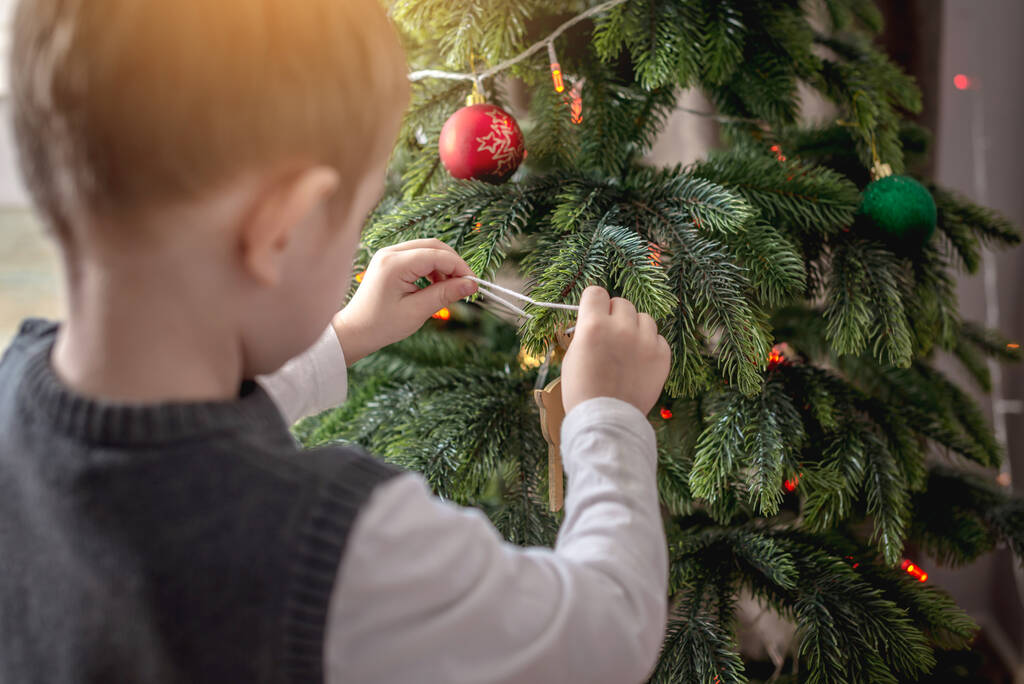 Sevimli küçük çocuk Noel ağacını oyuncaklar ve toplarla süslüyor. Yeni yıla hazırlık kavramı, rahat atmosfer ve şenlik havası. - Fotoğraf, Görsel