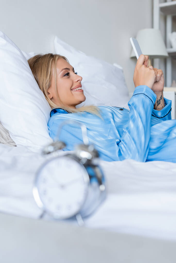 щаслива молода жінка використовує смартфон у спальні
  - Фото, зображення