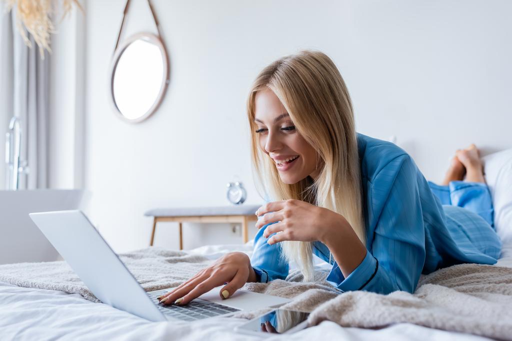 onnellinen nuori freelancer pyjamassa käyttäen kannettavaa makuuhuoneessa  - Valokuva, kuva