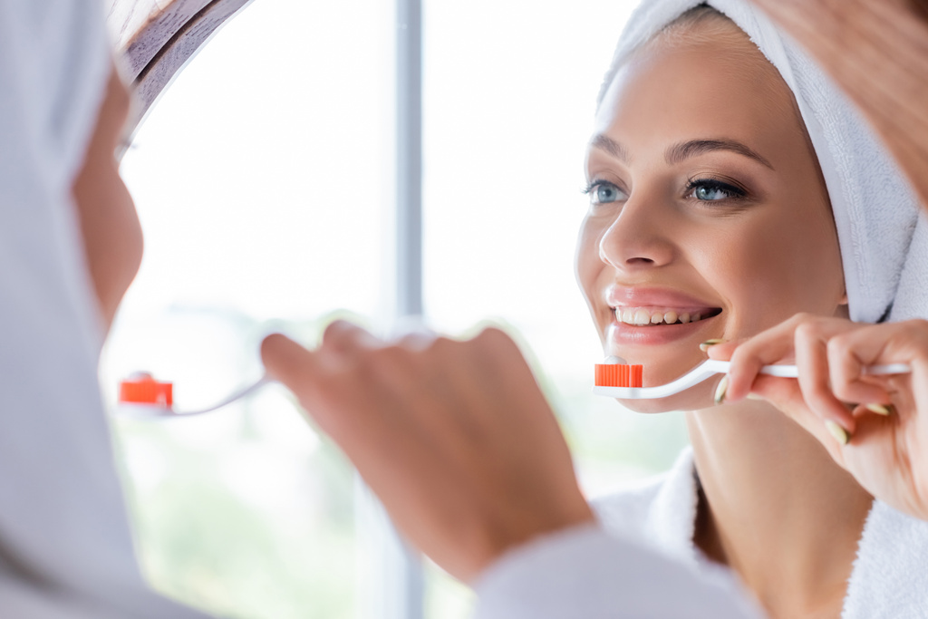 vrolijke vrouw poetsen tanden en kijken naar spiegel  - Foto, afbeelding