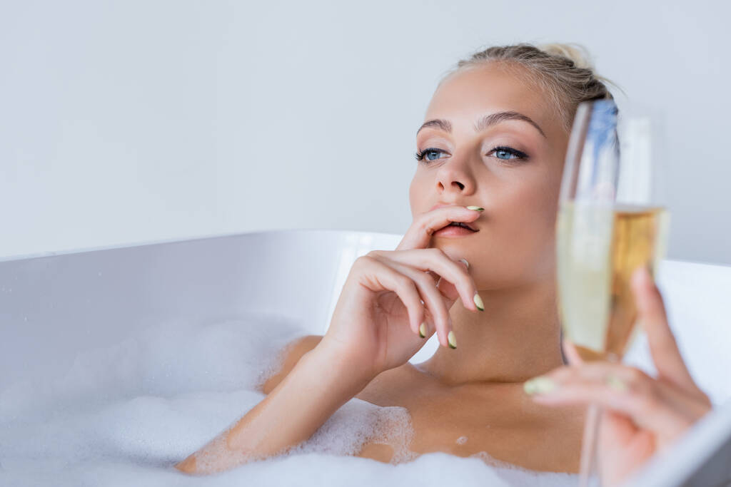 giovane donna sognante facendo il bagno e tenendo il bicchiere sfocato di champagne  - Foto, immagini