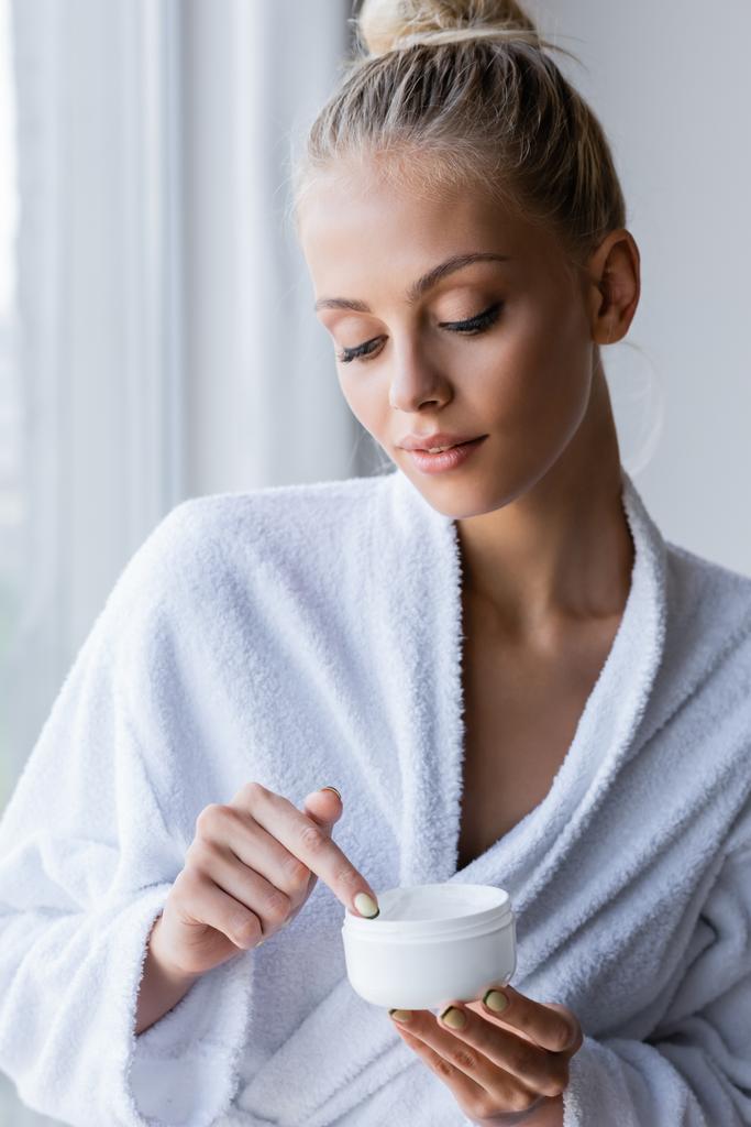 young woman in bathrobe holding container with cosmetic cream - Photo, Image