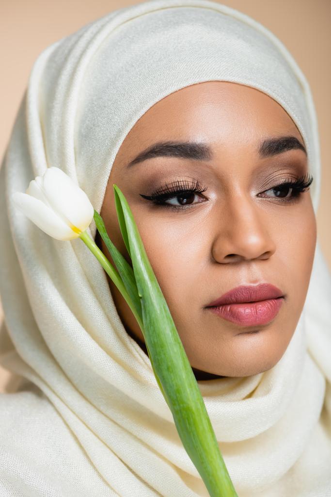 close up of young muslim woman in hijab near tulip isolated on beige  - Photo, Image