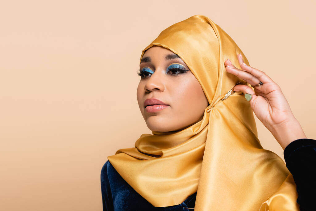 jeune femme musulmane en hijab jaune avec maquillage regardant loin isolé sur beige - Photo, image