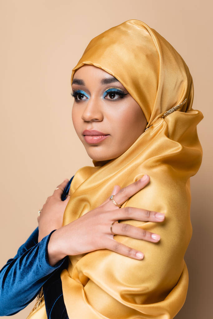 όμορφη μουσουλμάνα με κίτρινη χιτζάμπ ποζάροντας με σταυρωμένα χέρια απομονωμένη σε μπεζ - Φωτογραφία, εικόνα