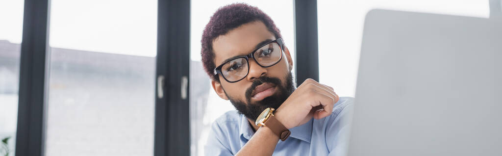 Mladý africký americký manažer při pohledu na rozmazaný notebook v kanceláři, banner  - Fotografie, Obrázek