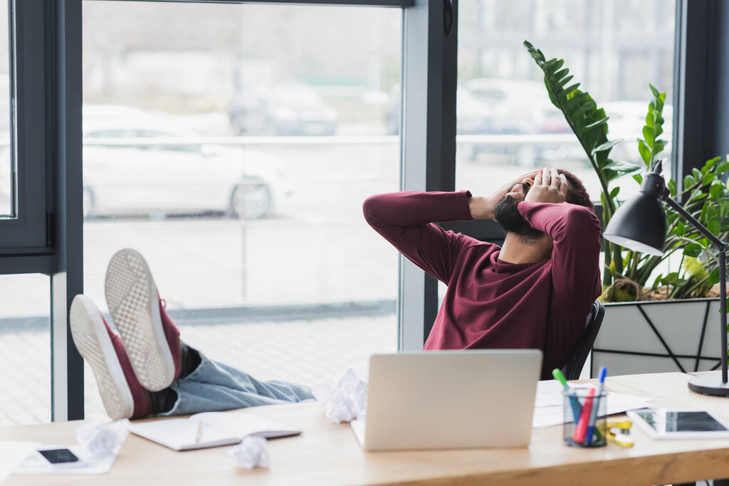 Cansado empresário afro-americano sentado perto de dispositivos e papel amassado no escritório  - Foto, Imagem
