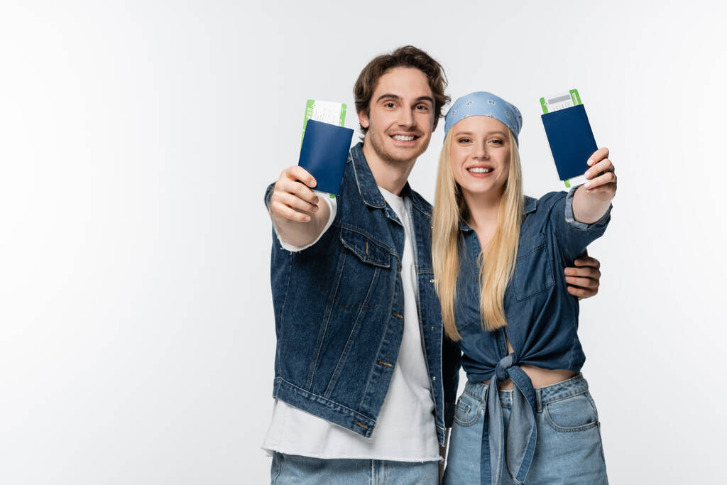 feliz jovem casal em roupas jeans mostrando passaportes com passagens aéreas isoladas em branco - Foto, Imagem