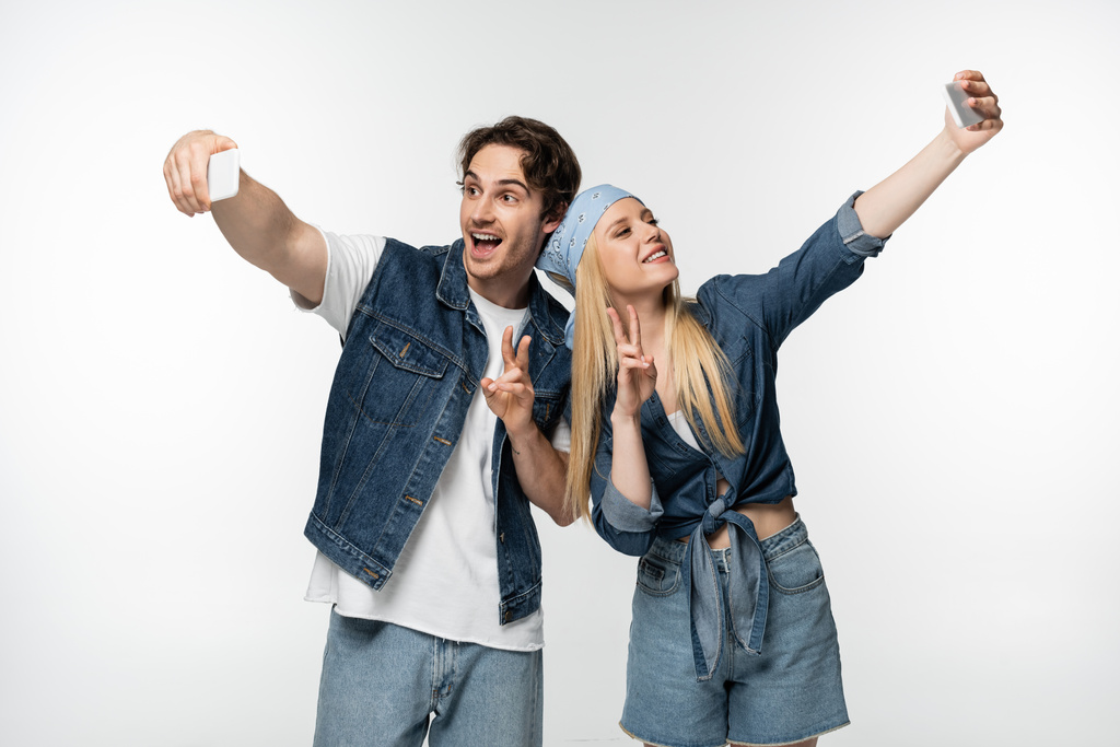 happy couple in denim clothing showing victory sings while taking selfie isolated on white - Photo, Image