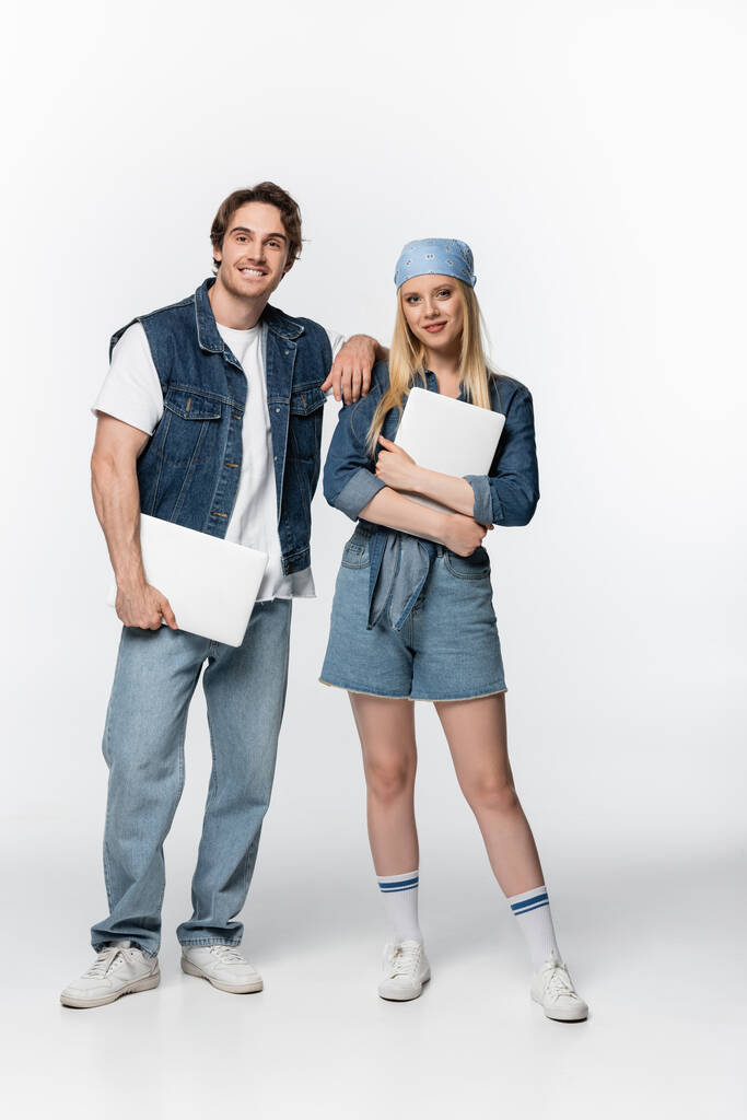 couple of happy freelancers in denim clothes holding laptops on white - Photo, Image