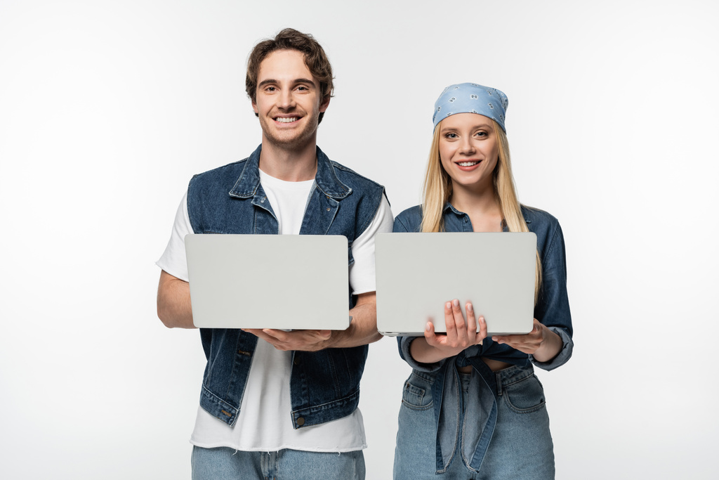 happy couple wearing denim clothes and holding laptops isolated on white - Photo, Image
