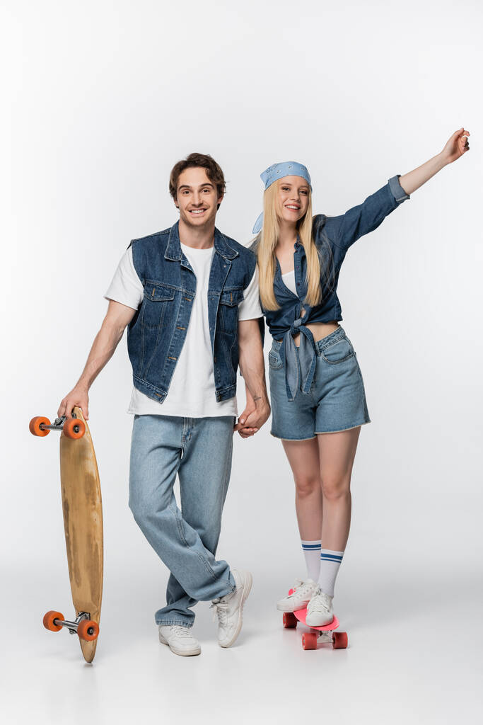 cheerful woman on penny board holding hands with boyfriend on white - Photo, Image