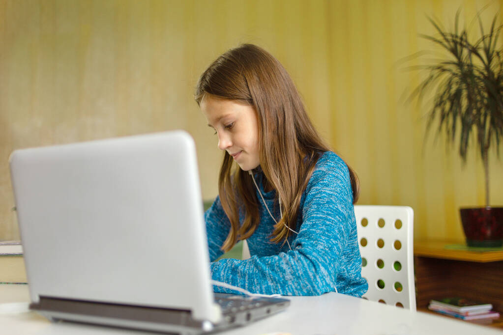 Η κοπέλα γράφει την εργασία της δασκάλας μπροστά στο λάπτοπ της. Ηλεκτρονική εκπαίδευση. Εκπαίδευση στο σπίτι - Φωτογραφία, εικόνα