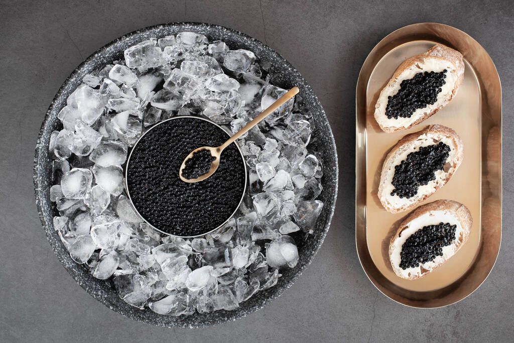 Caviale nero in lattina su ghiaccio e pane con burro su piatto d'oro - Foto, immagini