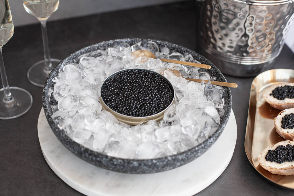 Schwarzer Kaviar in Dose auf Eis, Kaviarsandwich auf goldenem Teller, Champagner im Glas - Foto, Bild