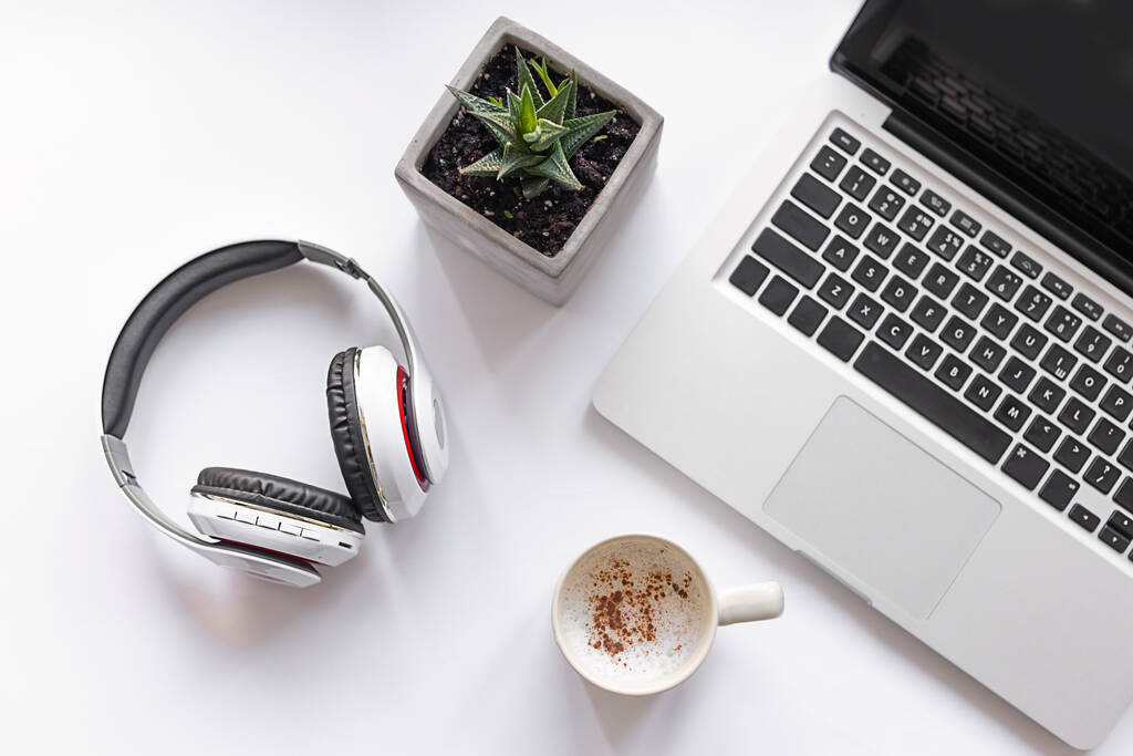 Fehér íróasztal laptoppal, zöld üzemmel, vezeték nélküli fejhallgatóval és kávé fehér háttérrel. Szabadúszó, online üzlet, online oktatás. Felülnézet, lapos fektetés - Fotó, kép