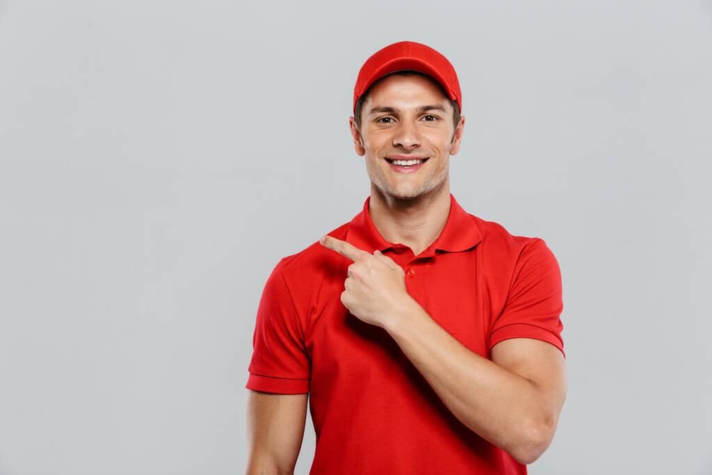 Young delivery man wearing uniform smiling and pointing finger aside isolated over white wall - Photo, Image