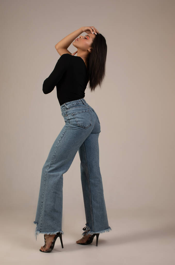 attractive stylish young african american woman in denim pants posing in studio on grey background - Photo, Image
