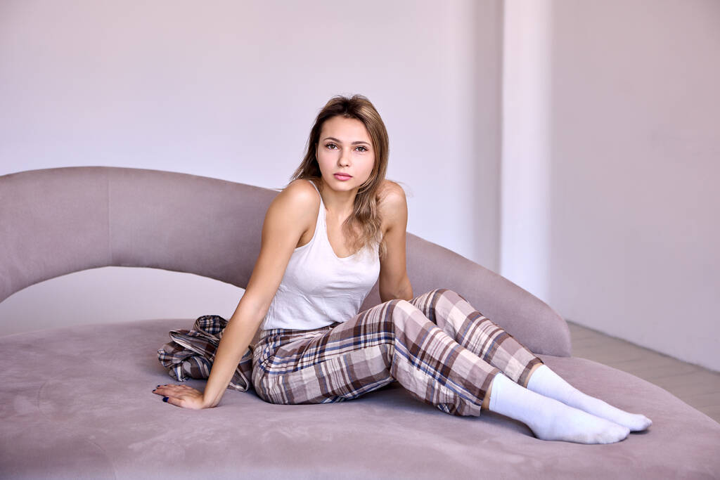 Slim donna in pantaloni a scacchi si siede sul letto in camera da letto. - Foto, immagini
