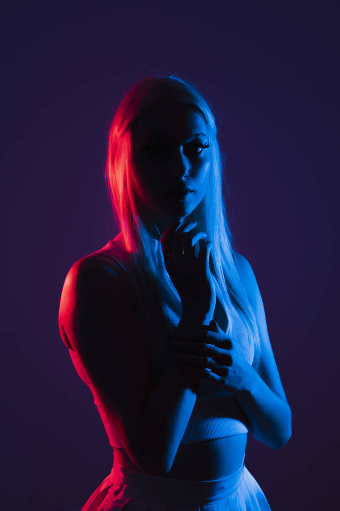 Porträt einer jungen Kanadierin in Sportbekleidung, die unter blauem und rotem Licht in einem dunklen Studio posiert - Foto, Bild