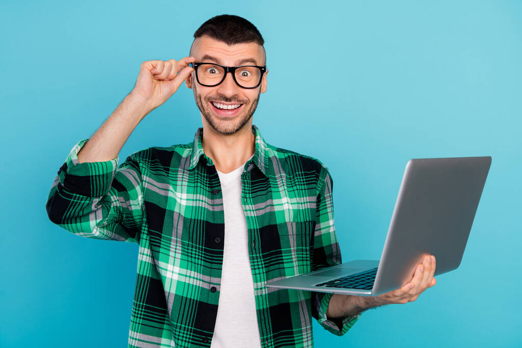 Foto de alegre hombre sorprendido feliz cogido de la mano programador portátil usar gafas aisladas en el fondo de color azul - Foto, imagen