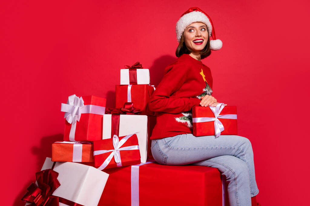 Photo de femme rêveuse brillante porter pull ornement assis tenant de nouveaux cadeaux de l'année à la recherche d'espace vide isolé fond de couleur rouge - Photo, image