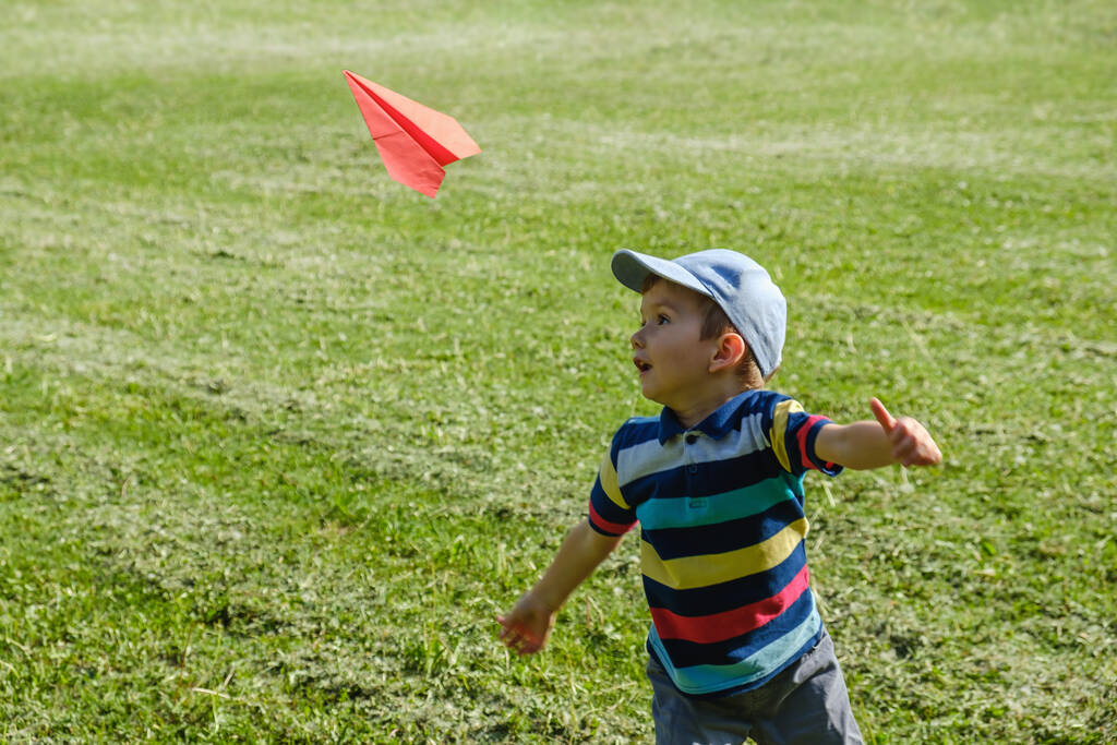 Jongen speelt met een toy rode vliegtuig in park op een zonnige zomerdag - Foto, afbeelding