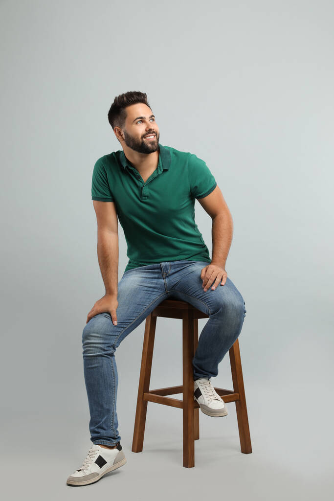 Handsome young man sitting on stool against light grey background - Photo, Image