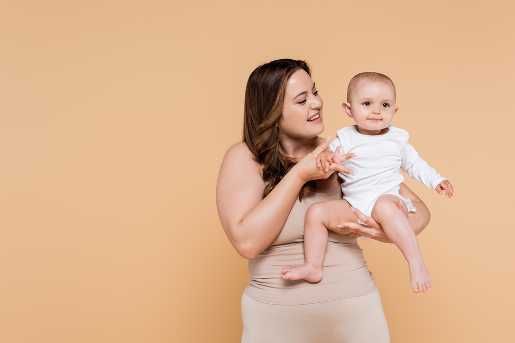 Happy plus velikost žena drží ruku dítěte izolované na béžové  - Fotografie, Obrázek