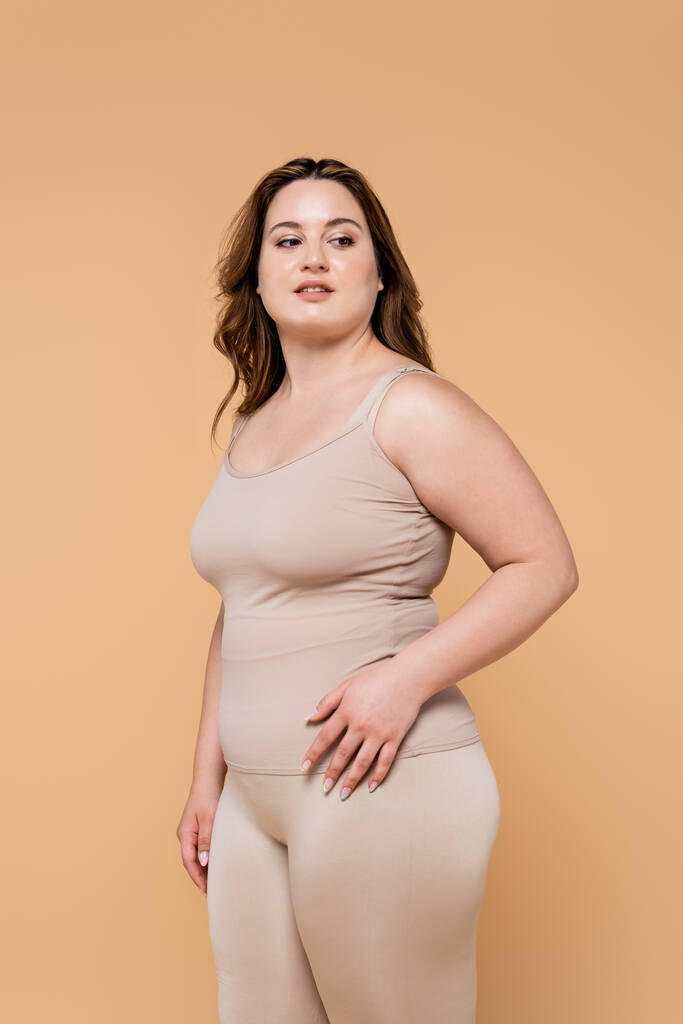 Mujer bonita con sobrepeso mirando hacia otro lado aislado en beige  - Foto, imagen