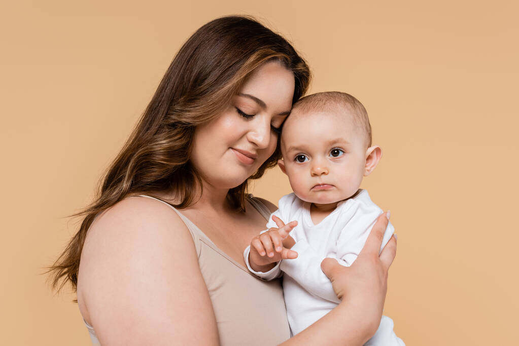 Body positive mother hugging baby daughter isolated on beige  - Photo, Image