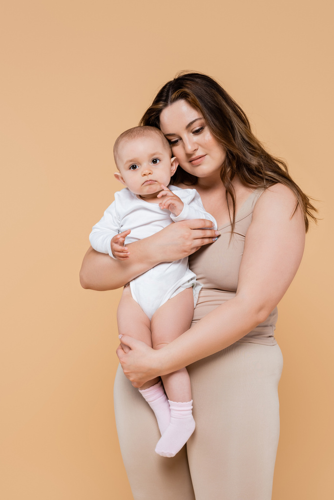 Plus size vrouw houden baby dochter geïsoleerd op beige  - Foto, afbeelding