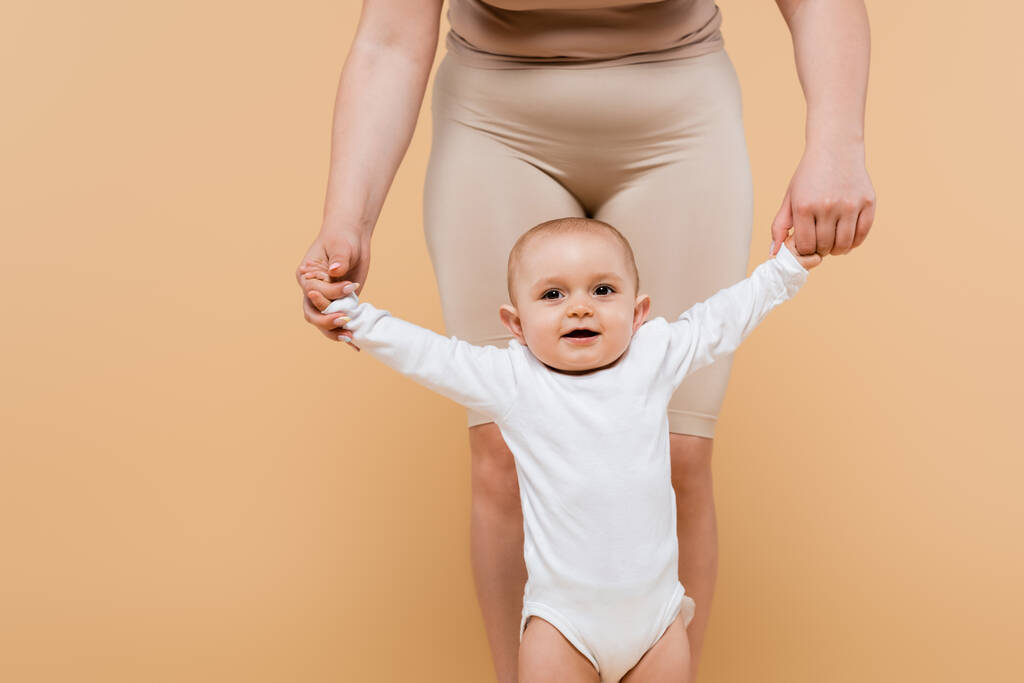 Body positive woman holding hands of child isolated on beige  - Photo, Image