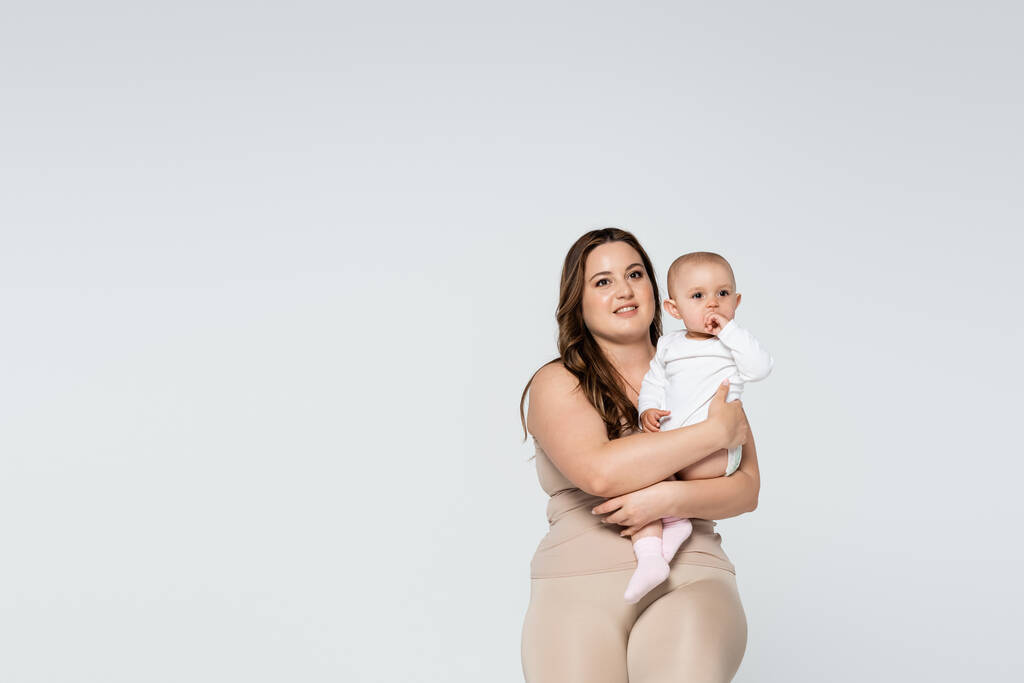 Счастливая женщина с избыточным весом держит ребенка изолированы на серый  - Фото, изображение