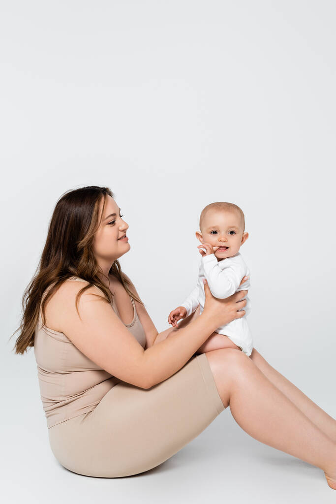 Jolie femme plus la taille tenant l'enfant avec doigt près de la bouche sur fond gris - Photo, image