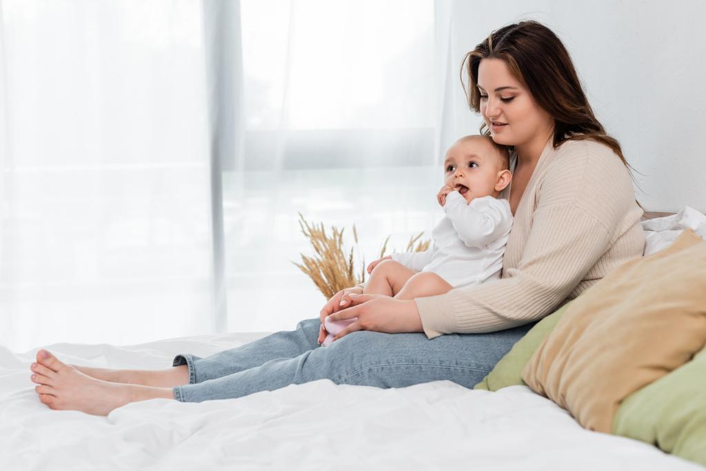 Positiver Körper positive Mutter berührt Beine der kleinen Tochter auf dem Bett  - Foto, Bild