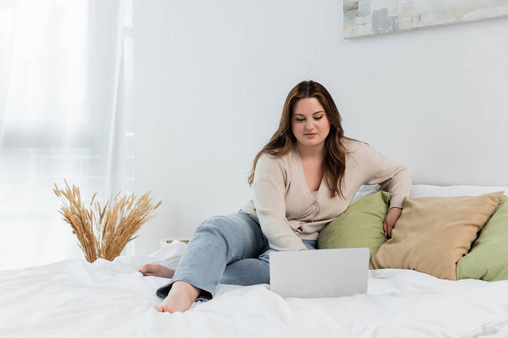 Barefoot plus size woman using laptop on bed at home  - Photo, Image